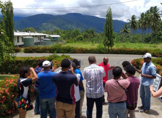 A group of researchers in PNG undergoing tablet data collection training, with mountain views in the background