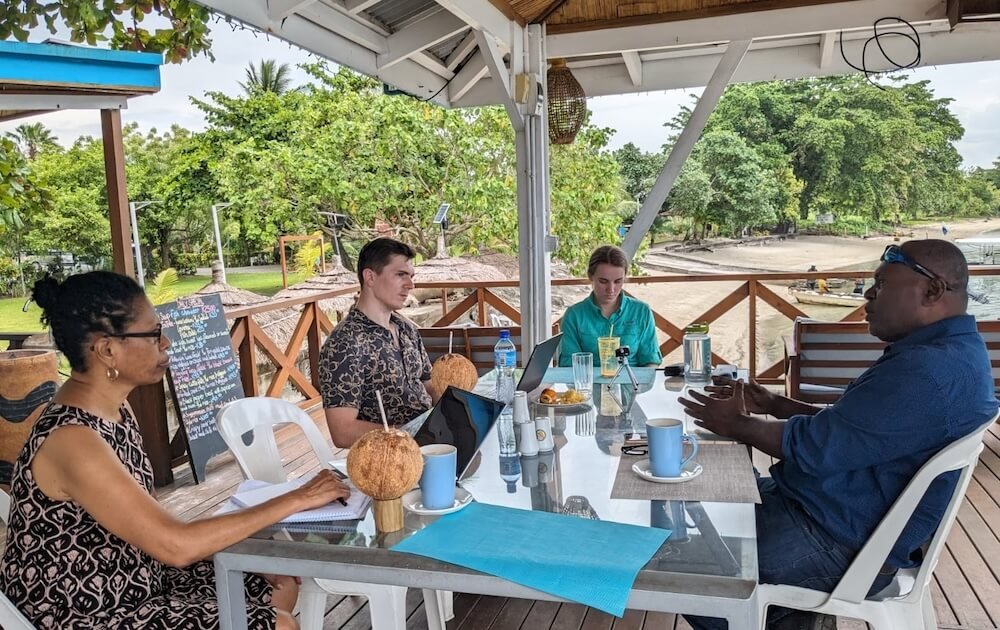 The Sustineo team interviewing a cocoa exporter outside under cover, with coconuts in hand