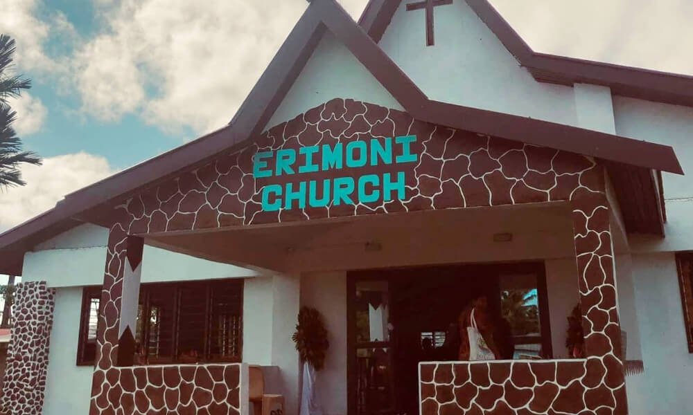 Photo of 'Erimoni Church' with white walls, high pitched roof, colourful tiled path leading up to the entrance.