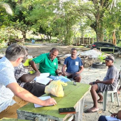 A focus group discussion with 7 participants around a table on sandy ground in Kaware, being facilitated by Dr Matt Allen
